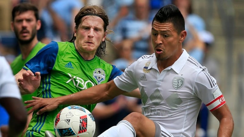 Sporting Kansas City midfielder Roger Espinoza, right, clears the ball away from Seattle...