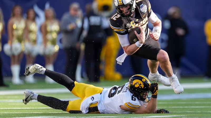 Missouri quarterback Brady Cook (12) runs the ball over Iowa defensive back Zach Lutmer (6)...